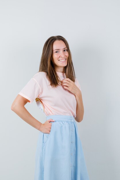 Mujer joven posando mientras está de pie en camiseta, falda y mirando alegre, vista frontal.