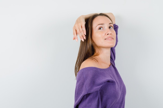 Mujer joven posando mientras mira hacia arriba en camisa violeta y se ve encantador.