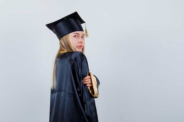 Mujer joven posando mientras mira a la cámara en uniforme de posgrado y parece encantador. .