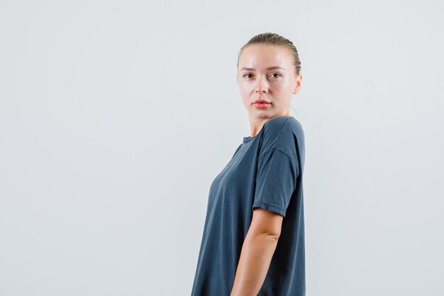 Mujer joven posando mientras mira en camiseta gris.