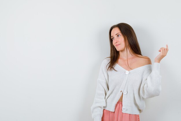 Mujer joven posando mientras mira a un lado en chaqueta de punto y falda elegante aislado