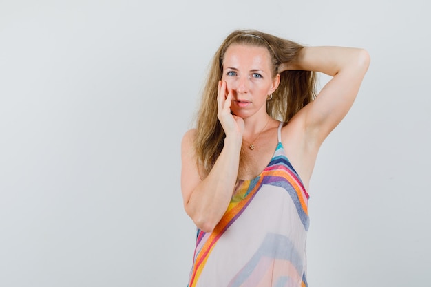 Foto gratuita mujer joven posando mientras sostiene la mano en el cabello con vestido de verano y se ve fascinante