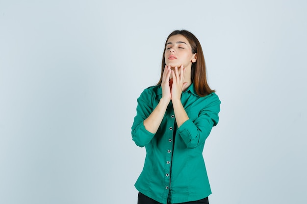 Mujer joven posando mientras toca la piel de su barbilla con camisa verde y luciendo elegante, vista frontal.