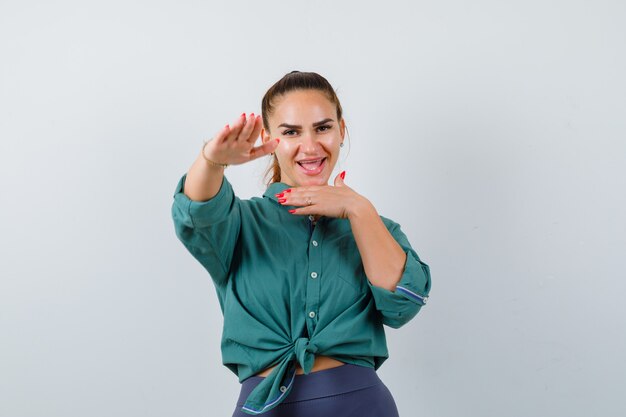 Mujer joven posando con la palma hacia afuera para detenerse en camisa verde y lucir feliz. vista frontal.