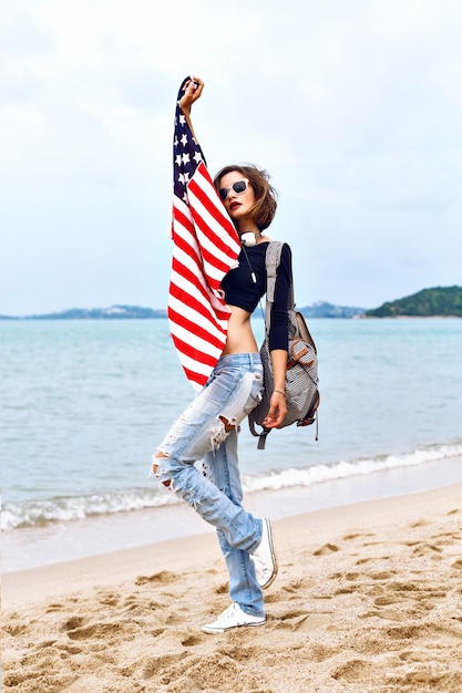 Mujer joven posando en la playa escuchando música en sus elegantes auriculares grandes