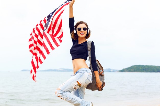 Mujer joven posando en la playa escuchando música en sus elegantes auriculares grandes