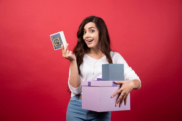 Mujer joven posando con presente sobre fondo rojo. Foto de alta calidad