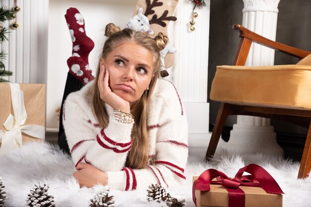 Una mujer joven posando con un regalo de Navidad y acostada sobre una alfombra.