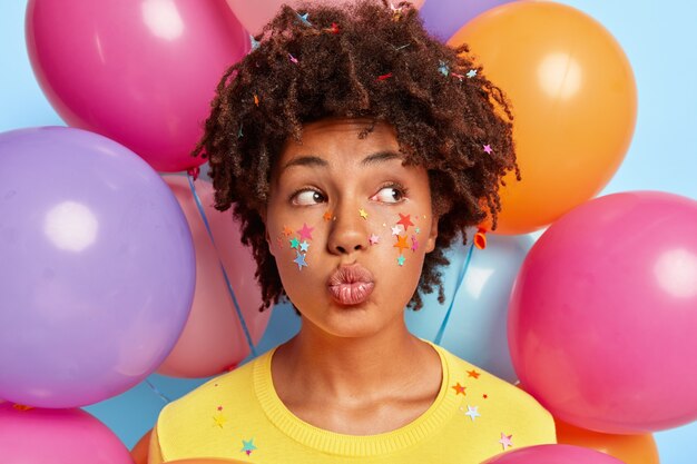 Mujer joven posando rodeada de globos de colores de cumpleaños