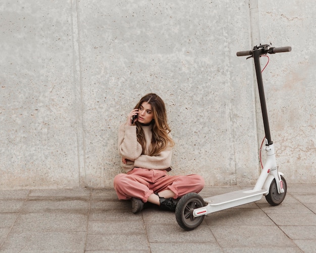 Mujer joven posando con un scooter eléctrico