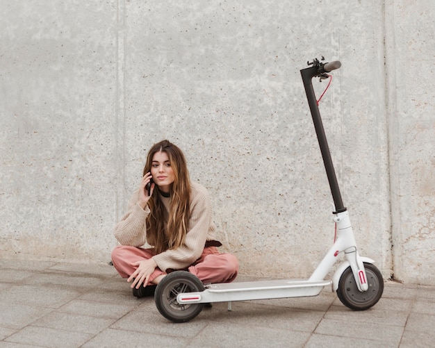Mujer joven posando con un scooter eléctrico
