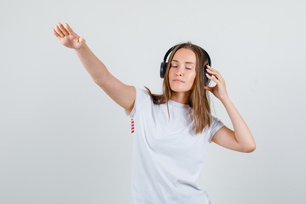 Mujer joven posando sosteniendo auriculares en camiseta blanca y mirando relajado