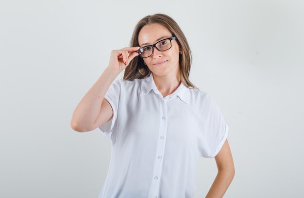 Mujer joven posando sosteniendo sus gafas en camiseta blanca