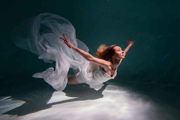 Mujer joven posando sumergido bajo el agua con un vestido fluido