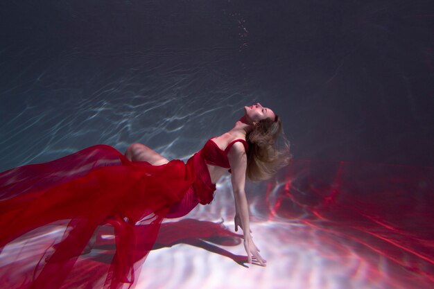 Mujer joven posando sumergido bajo el agua con un vestido fluido