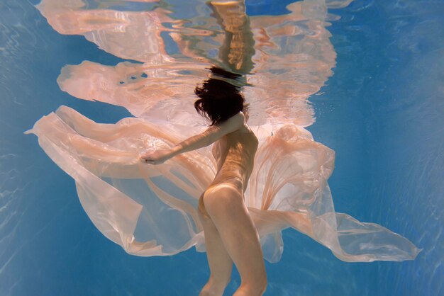 Mujer joven posando sumergido bajo el agua con un vestido fluido