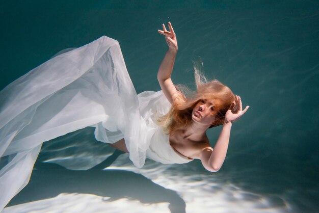 Mujer joven posando sumergido bajo el agua con un vestido fluido