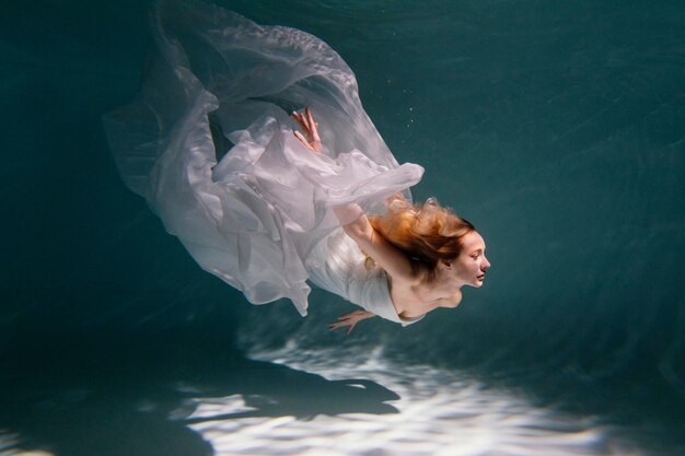 Mujer joven posando sumergido bajo el agua con un vestido fluido