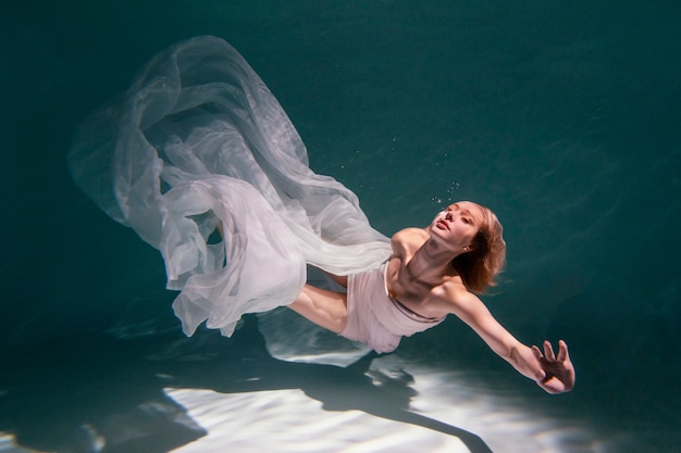 Mujer joven posando sumergido bajo el agua con un vestido fluido