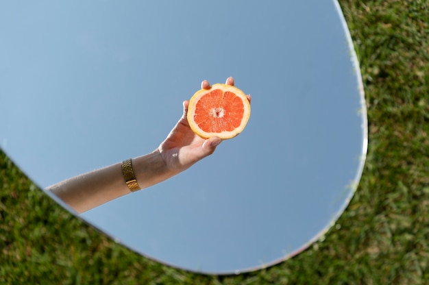 Foto gratuita mujer joven, posar, con, pomelo, en, el, espejo, en, pasto o césped