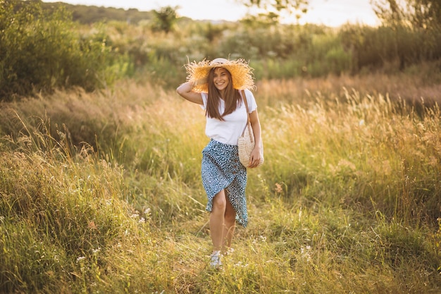 Foto gratuita mujer joven, posición, con, bolsa, en, sombrero grande, en, campo