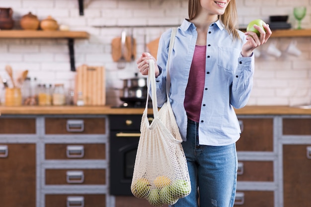 Mujer joven positiva con bolsa reutilizable con frutas eco