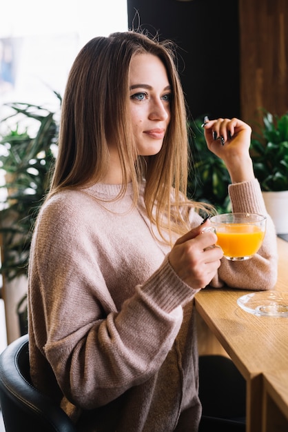 Foto gratuita mujer joven positiva elegante que sostiene la taza de bebida en el contador de la barra en café