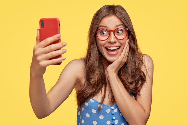 Mujer joven positiva con gafas posando contra la pared amarilla