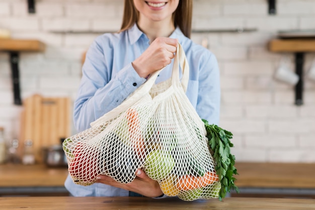 Mujer joven positiva que sostiene la bolsa reutilizable con verduras