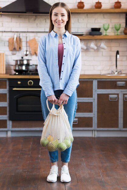 Mujer joven positiva que sostiene el bolso reutilizable con las frutas