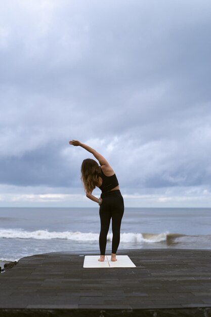 Mujer joven practica yoga en una hermosa playa al amanecer. Cielo azul, océano, olas, proximidad a la naturaleza, unidad con la naturaleza.