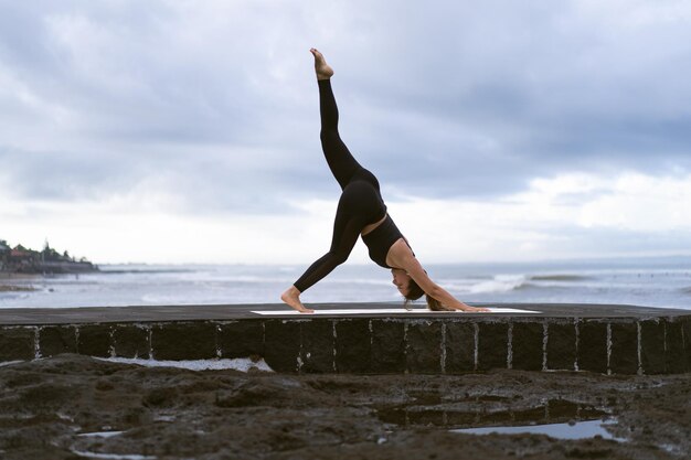 Mujer joven practica yoga en una hermosa playa al amanecer. Cielo azul, océano, olas, proximidad a la naturaleza, unidad con la naturaleza.