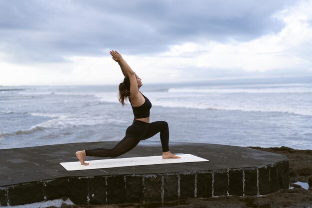 Mujer joven practica yoga en una hermosa playa al amanecer. Cielo azul, océano, olas, proximidad a la naturaleza, unidad con la naturaleza.