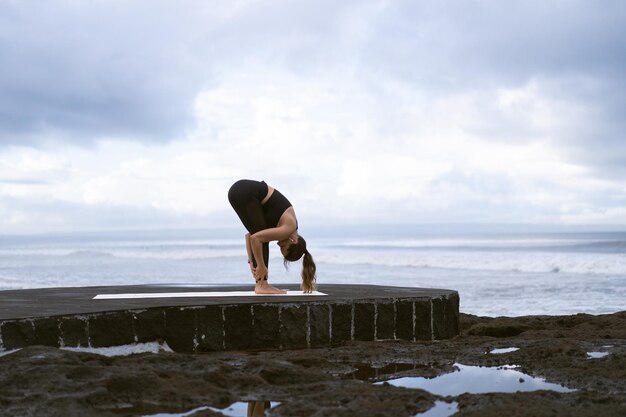 Mujer joven practica yoga en una hermosa playa al amanecer. Cielo azul, océano, olas, proximidad a la naturaleza, unidad con la naturaleza.