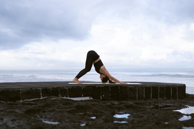 Mujer joven practica yoga en una hermosa playa al amanecer. Cielo azul, océano, olas, proximidad a la naturaleza, unidad con la naturaleza.