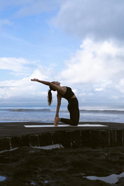 Mujer joven practica yoga en una hermosa playa al amanecer. Cielo azul, océano, olas, proximidad a la naturaleza, unidad con la naturaleza.