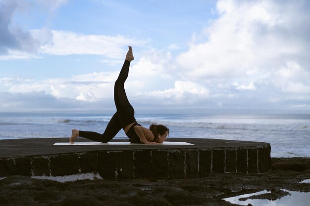 Mujer joven practica yoga en una hermosa playa al amanecer. Cielo azul, océano, olas, proximidad a la naturaleza, unidad con la naturaleza.