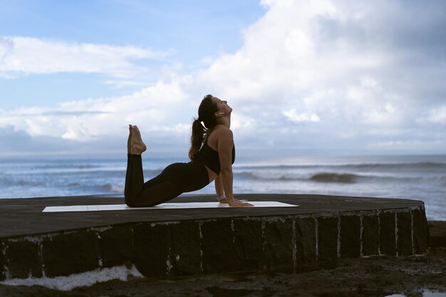 Mujer joven practica yoga en una hermosa playa al amanecer. Cielo azul, océano, olas, proximidad a la naturaleza, unidad con la naturaleza.