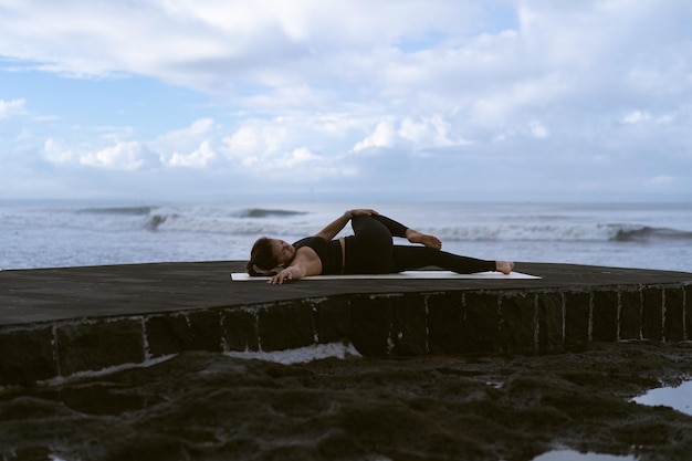 Mujer joven practica yoga en una hermosa playa al amanecer. Cielo azul, océano, olas, proximidad a la naturaleza, unidad con la naturaleza.