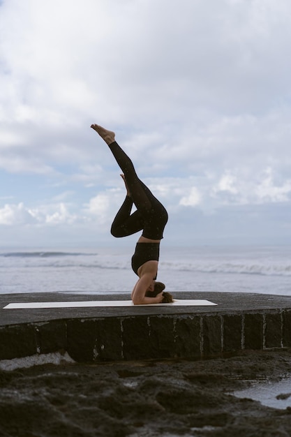 Mujer joven practica yoga en una hermosa playa al amanecer. Cielo azul, océano, olas, proximidad a la naturaleza, unidad con la naturaleza.