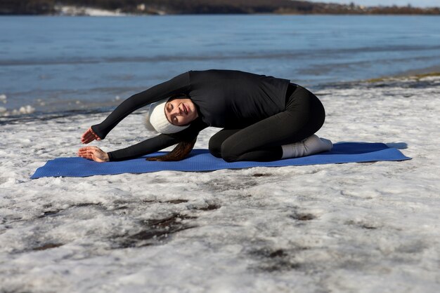 Mujer joven practicando yoga al aire libre durante el invierno en la playa