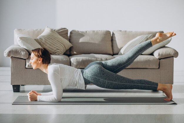 Mujer joven practicando yoga en casa en mat