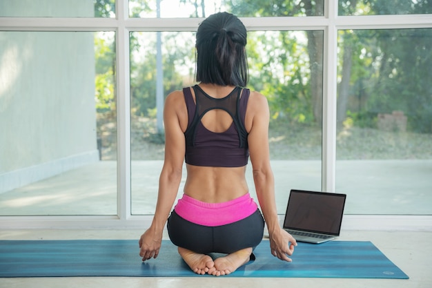 Mujer joven practicando yoga, haciendo ejercicio, pose sentada, haciendo ejercicio, vistiendo ropa deportiva, interior de cuerpo entero, estudio de yoga, vista trasera. Bienestar, concepto de atención plena, hacer ejercicio en casa sentado.