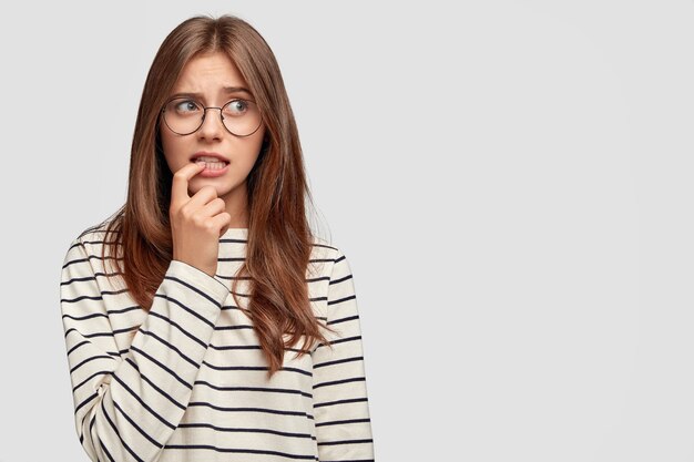 Mujer joven preocupada con gafas posando contra la pared blanca