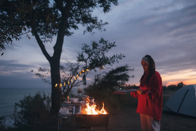 Mujer joven preparando comida a la parrilla junto al mar