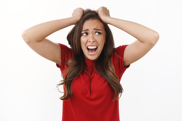 Foto gratuita mujer joven con problemas, insegura y presa del pánico de cintura para arriba, se siente presionada y tensa, grita de tristeza y dolor, recibe una mala puntuación decepcionada, se saca el pelo de la cabeza, mira hacia otro lado con el ceño fruncido