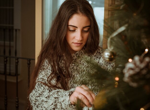 Mujer joven que adorna el árbol de navidad en casa