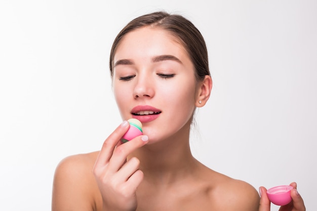 Mujer joven que aplica bálsamo labial higiénico en la pared blanca