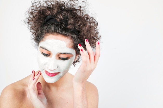 Foto gratuita mujer joven que aplica la crema cosmética en su cara contra el fondo blanco