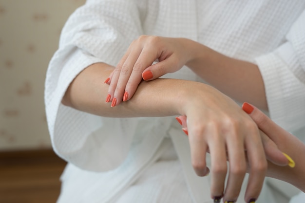 Mujer joven que aplica con crema hidratante blanca del dedo a mano.